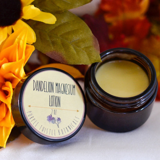 An up- close picture of an open amber glass jar. Inside the jar is yellow lotion.  Behind the jar are red, orange, and yellow flowers. 